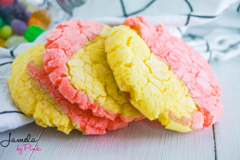 Lemon crinkle cookies with strawberry on a white towel with black lines and a jar of jelly beans in the distance