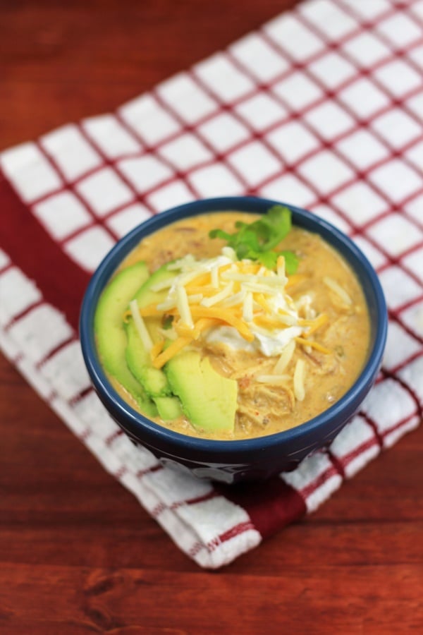 blå skål på en röd och vit kökshandduk med keto kyckling chili toppad med avokado, ost, surkräm och koriander