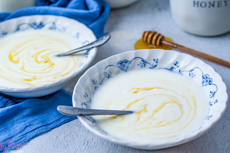 2 bowls of instant pot yogurt with spoons in them honey in the background and a blue cheesecloth