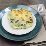 Plated Instant Pot Chicken Spinach Artichoke Lasagna on a white plate, sitting on a green plate, with a tan napkin and fork.
