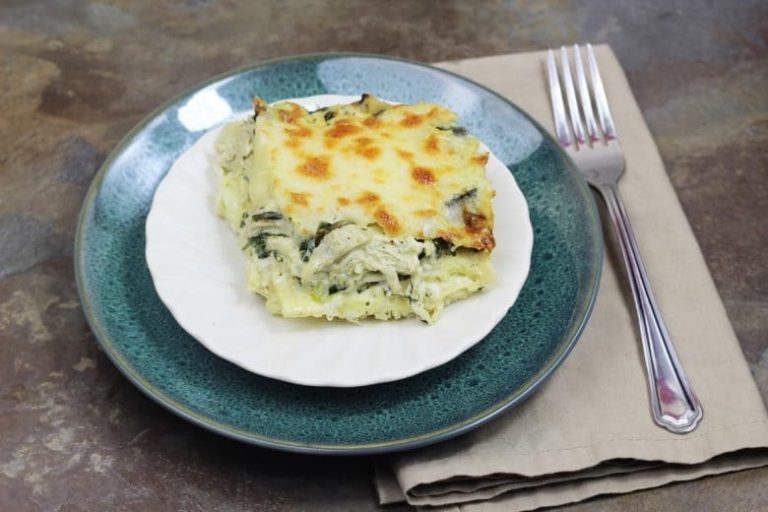 Plated Instant Pot Chicken Spinach Artichoke Lasagna on a white plate, sitting on a green plate, with a tan napkin and fork.