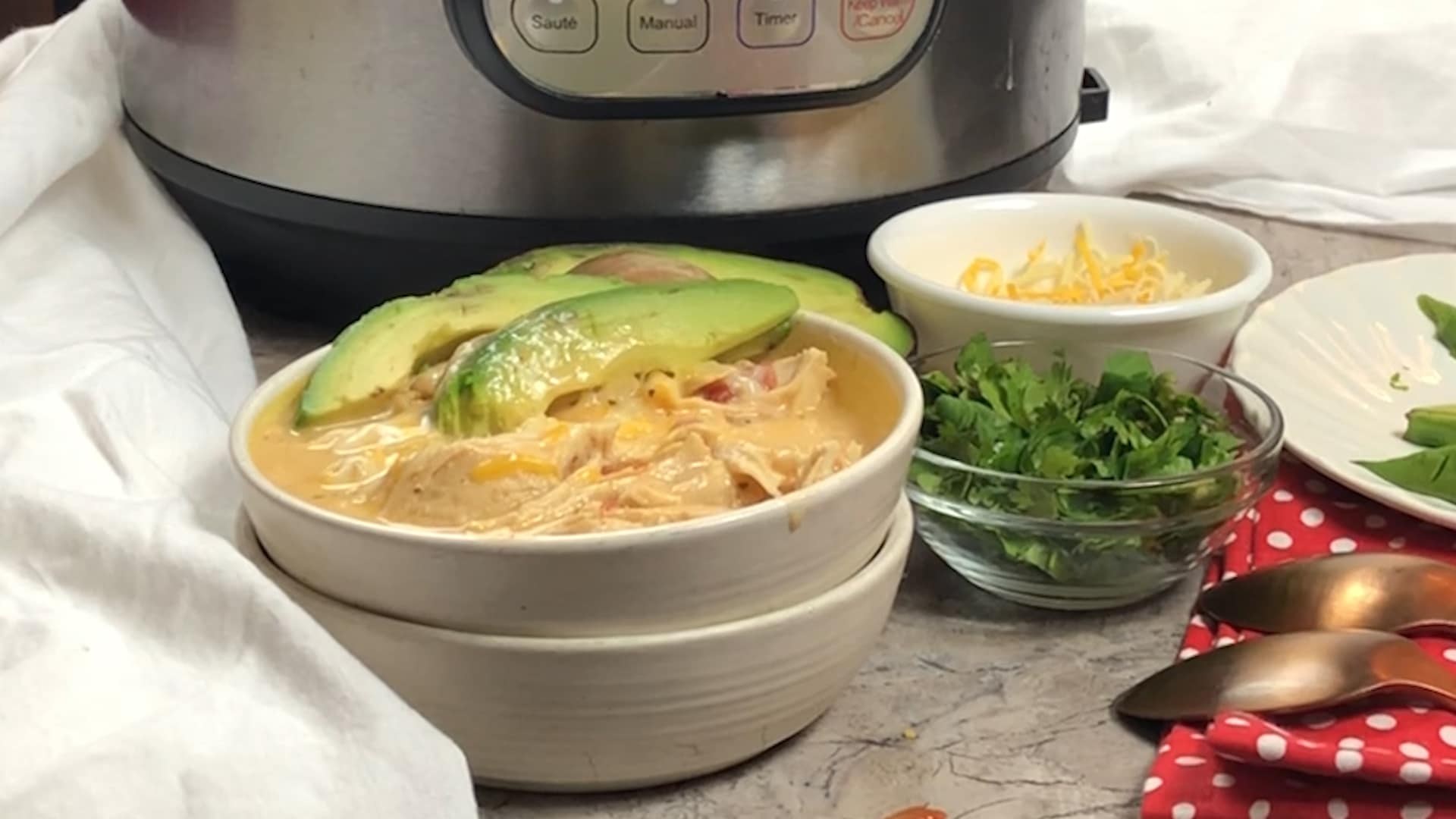 instant pot with a white bowl in front of it with white chicken chili in it with 2 avocado slices on it