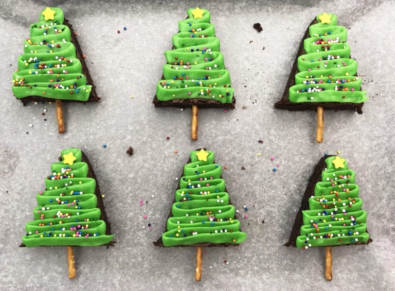 christmas tree brownies on a baking sheet with parchment paper, decorated with green icing, sprinkles and a star