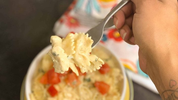 cajun chicken pasta in a white bowl on a yellow plate with person holding pasta above it on a fork