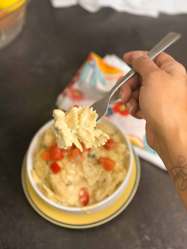 cajun chicken pasta in a white bowl on a yellow plate with person holding pasta above it on a fork