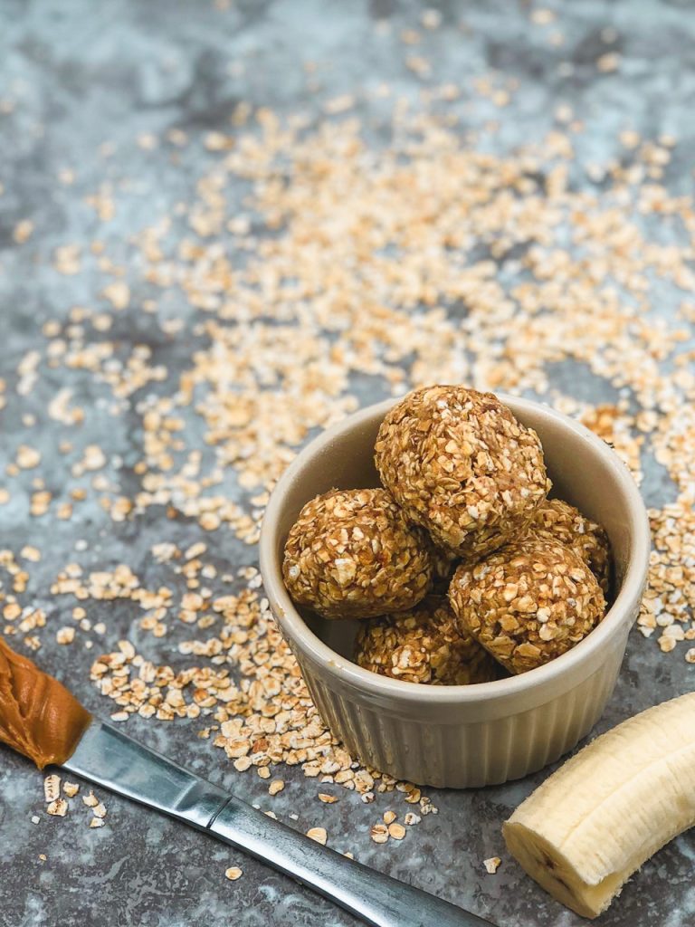 oatmeal balls in a tan ramekin with a silver peanut bitter covered knife and half a banana