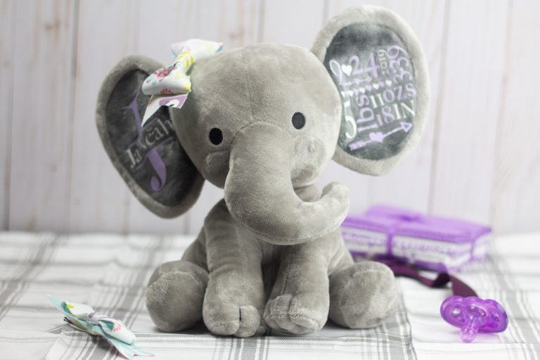 personalized stuffed animal with fabric bow and purple and white text on the ears