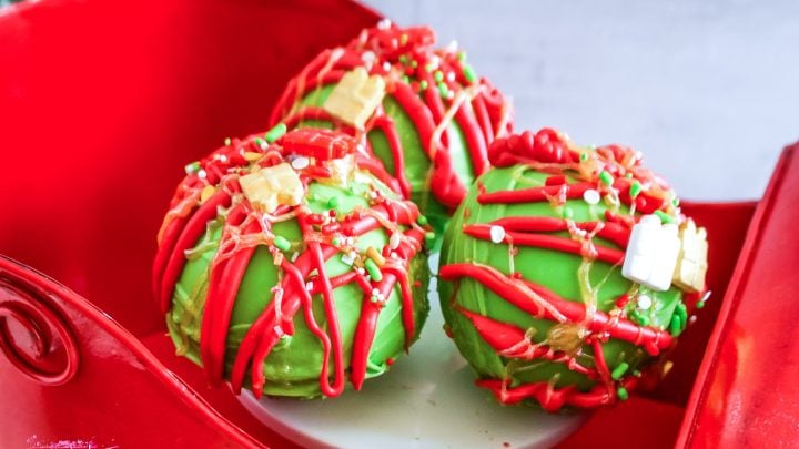 red and green grinch inspired hot chocolate bombs sitting in a red sleigh