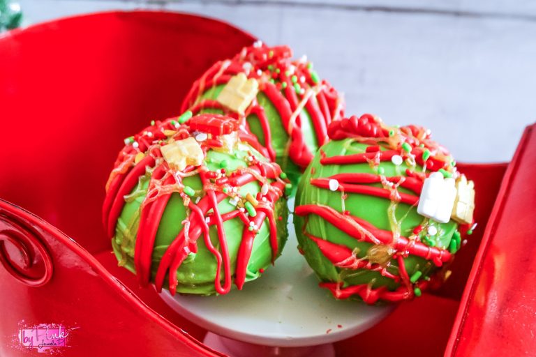 red and green grinch inspired hot chocolate bombs sitting in a red sleigh