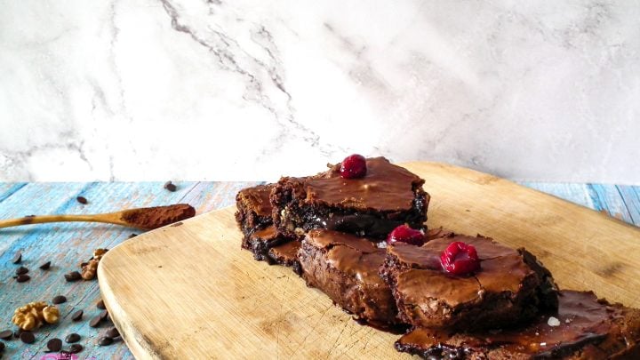 three walnut brownies with cherries on wooden cutting board from side angle