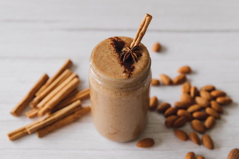 cinnamon almond butter in a jae=r with a cinnamon stick sticking out. more cinnamon sticks and almonds are in the background
