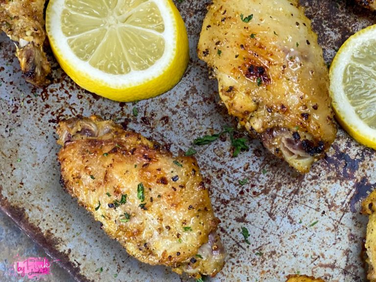 top close up of lemon pepper wins made in the air fryer, on a baking sheet with lemon slices