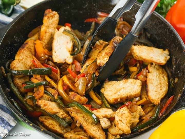 chicken fajitas in a cast iron skillet with tongs removing some